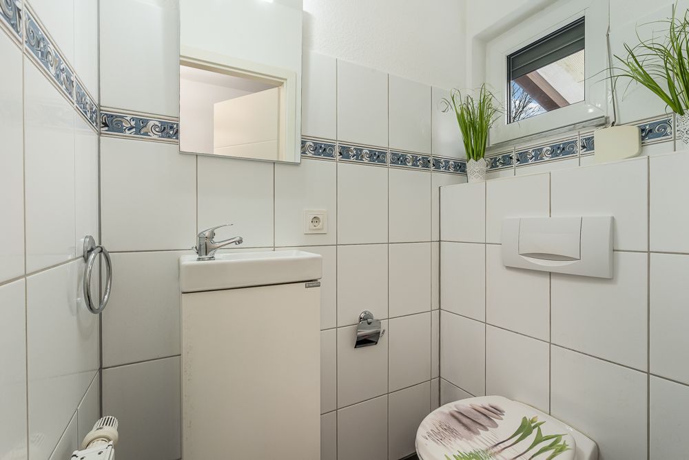Kleines, weiß gefliestes Bad mit Waschbecken, Toilette und kleinem Fenster.