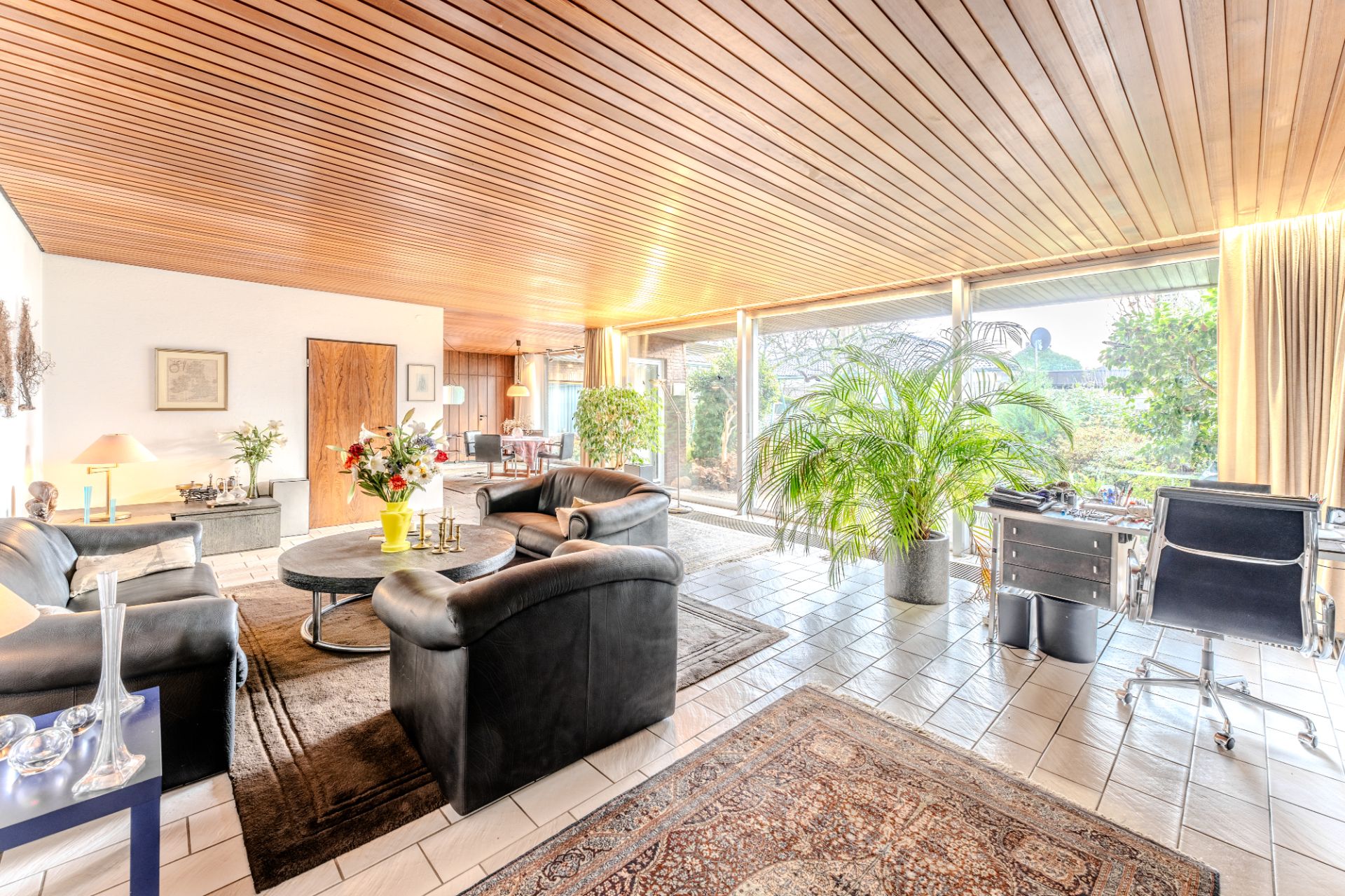 Helles Wohnzimmer mit Ledersesseln, Holzboden, großen Fenstern und vielen Pflanzen.