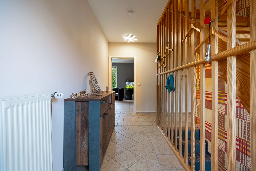 Flur mit Holztreppe, Holzgeländer und Kommode, Türöffnung im Hintergrund.