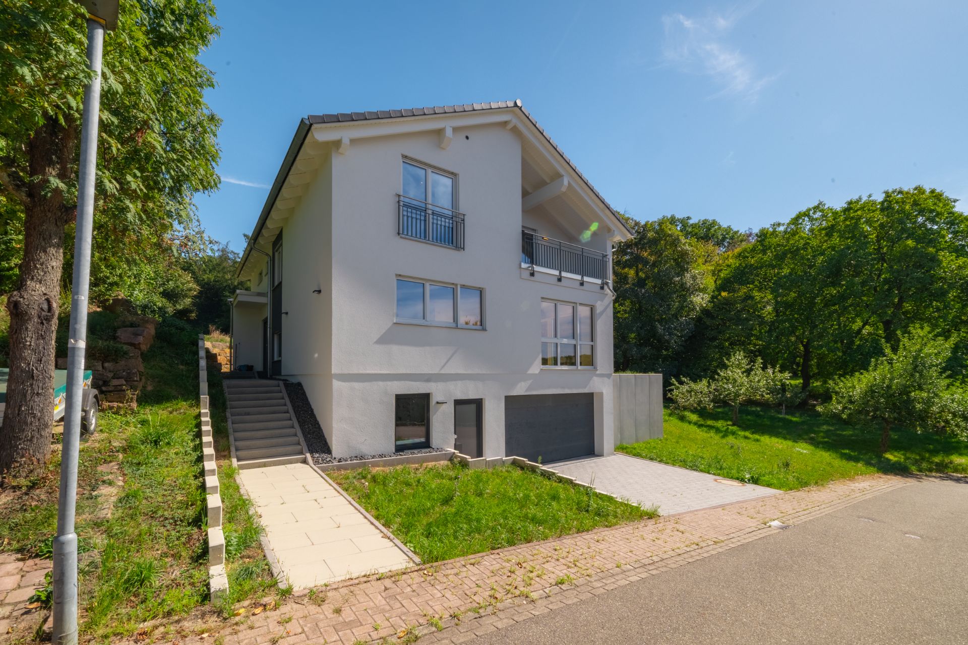 Modernes, weißes Einfamilienhaus mit Einfahrt, Garage und Garten an einer ruhigen Straße.