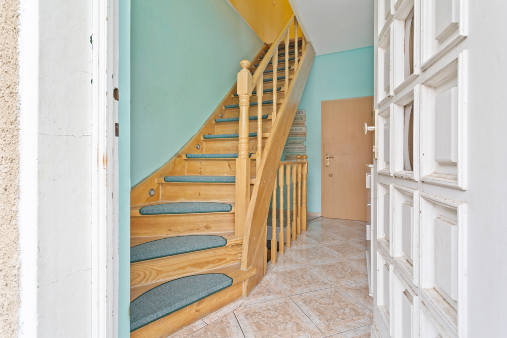 Eingangsbereich mit offener Holztreppe und türkis gestrichenen Wänden.
