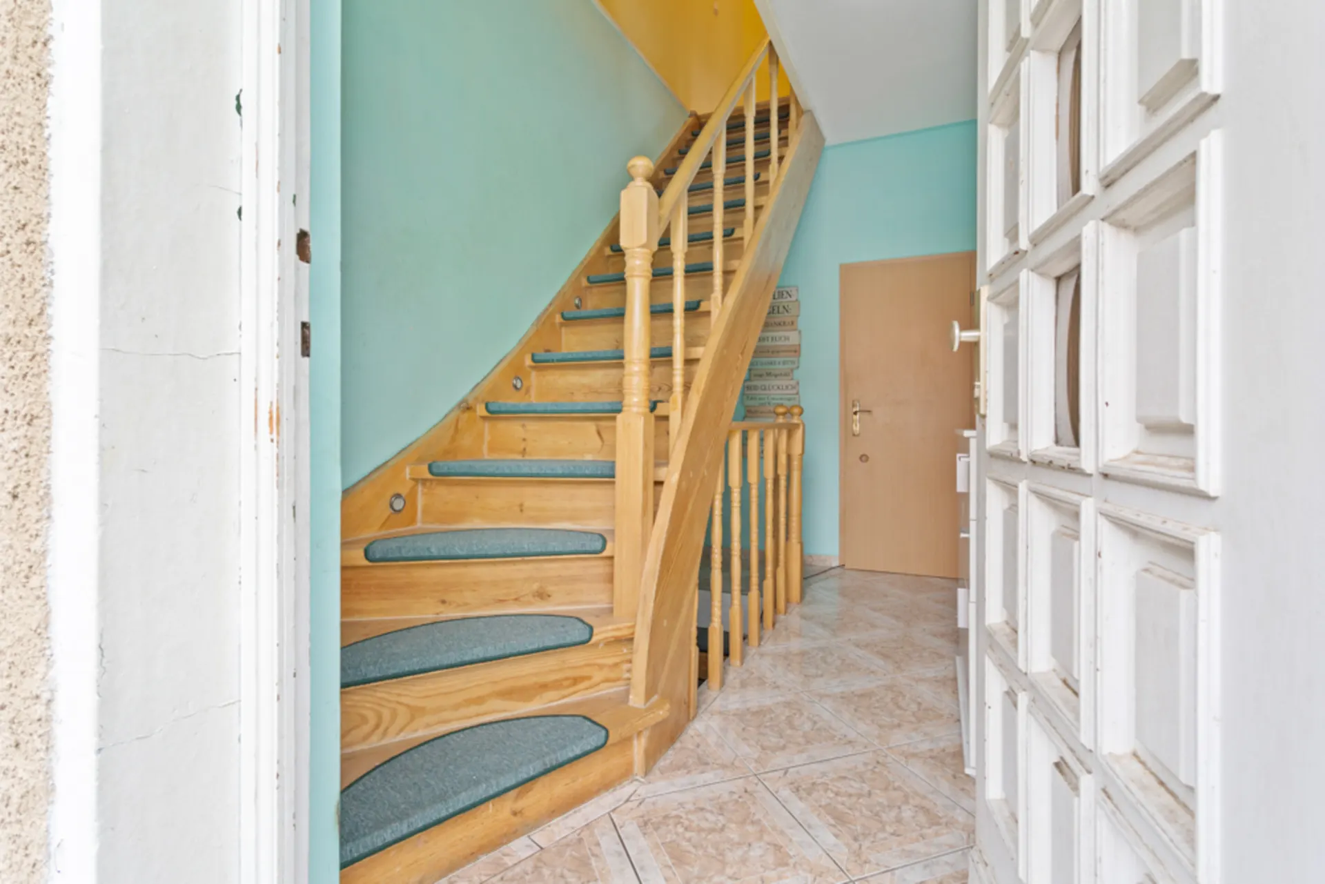 Eingangsbereich mit offener Holztreppe und türkis gestrichenen Wänden.