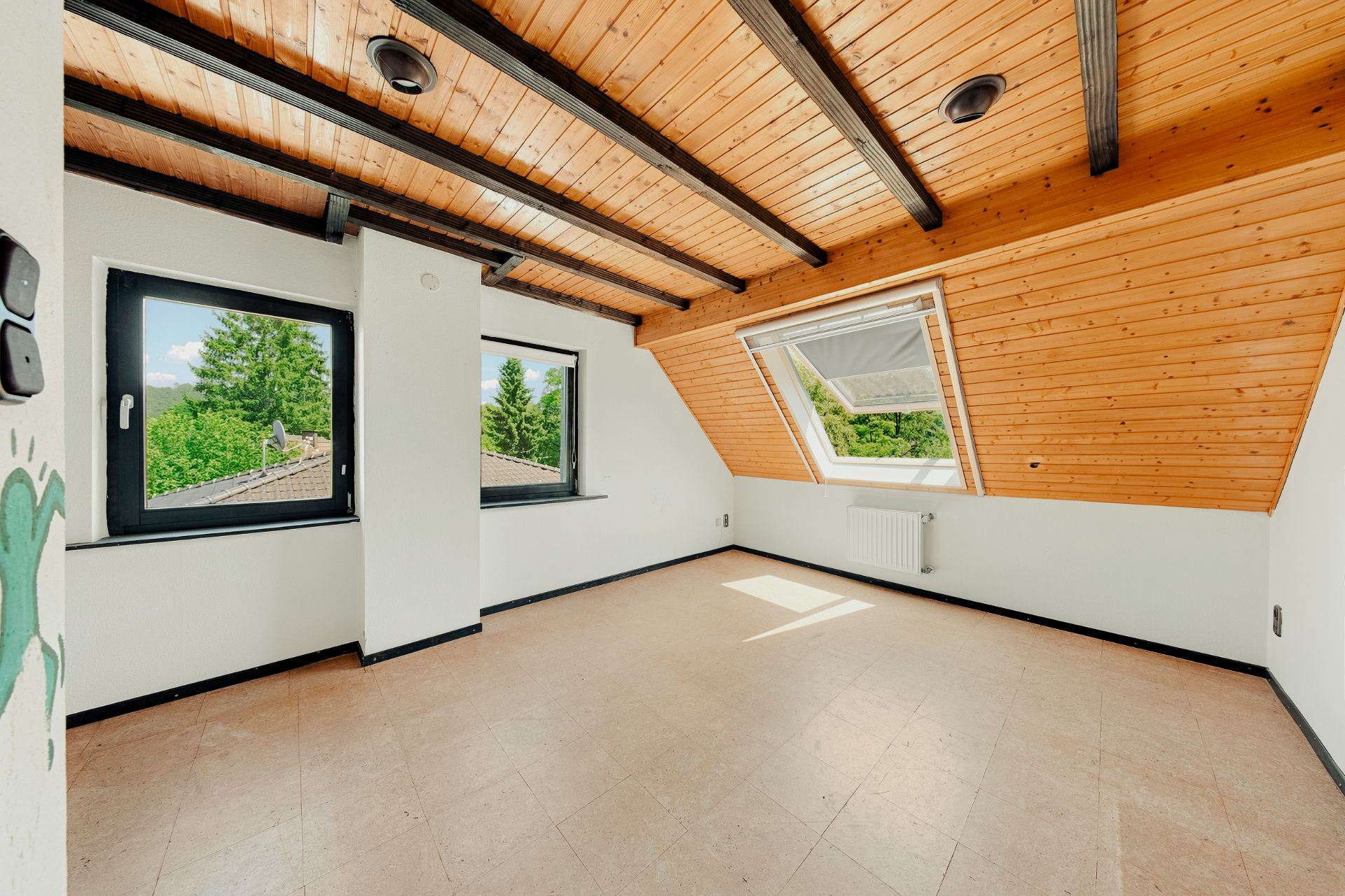 Heller Dachraum mit zwei Fenstern, Holzdecke und schräger Wandverkleidung.