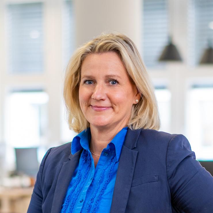 Frau mit blonder Schulterlangen Haaren im blauen Blazer in einem hellen Raum.