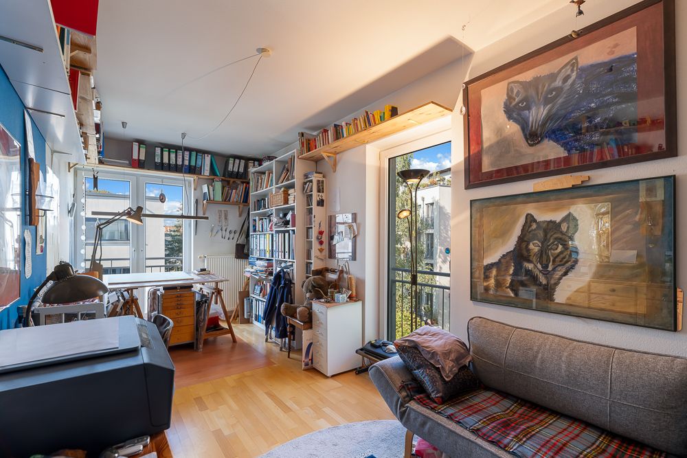 Helles Arbeitszimmer mit Sofa, Schreibtisch, Regalen und zwei Wolfsbildern an der Wand.