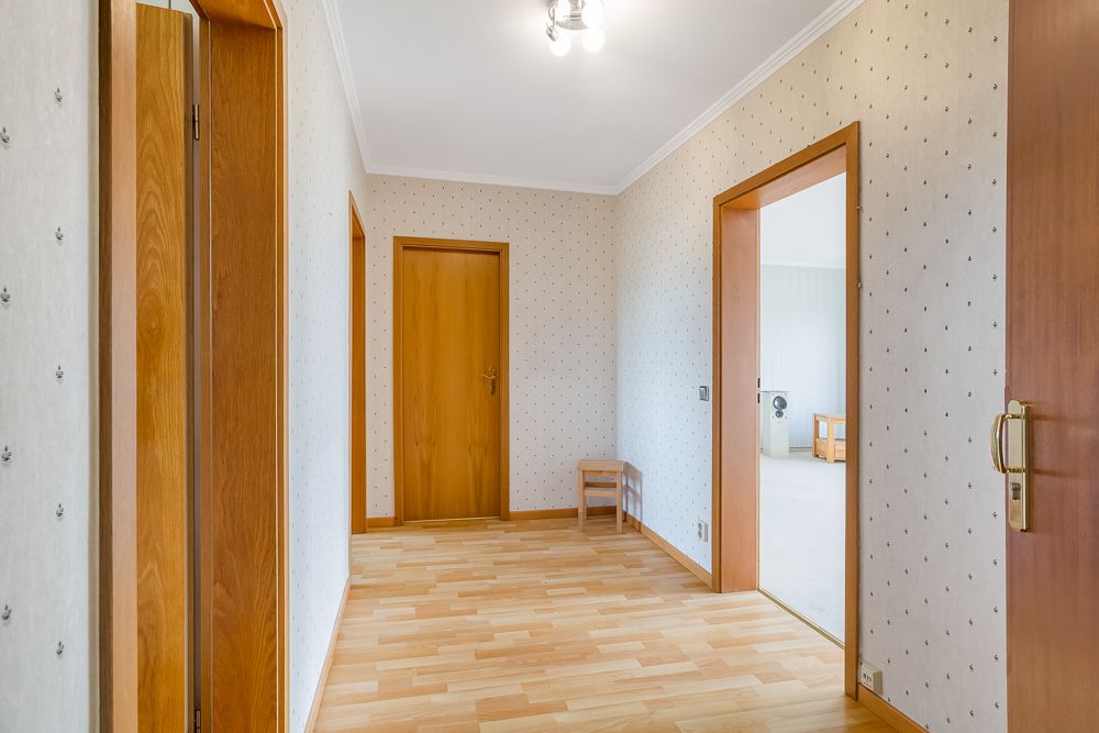 Heller Flur mit Holztüren, gemusterter Tapete und einem kleinen Stuhl an der Wand.