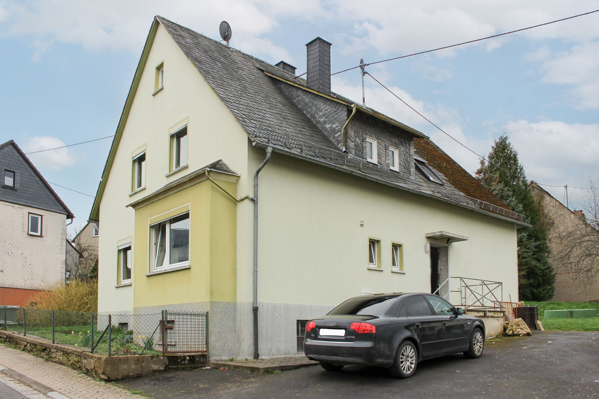 Zweistöckiges Wohnhaus mit schrägem Dach und schwarzem Auto vor der Einfahrt.