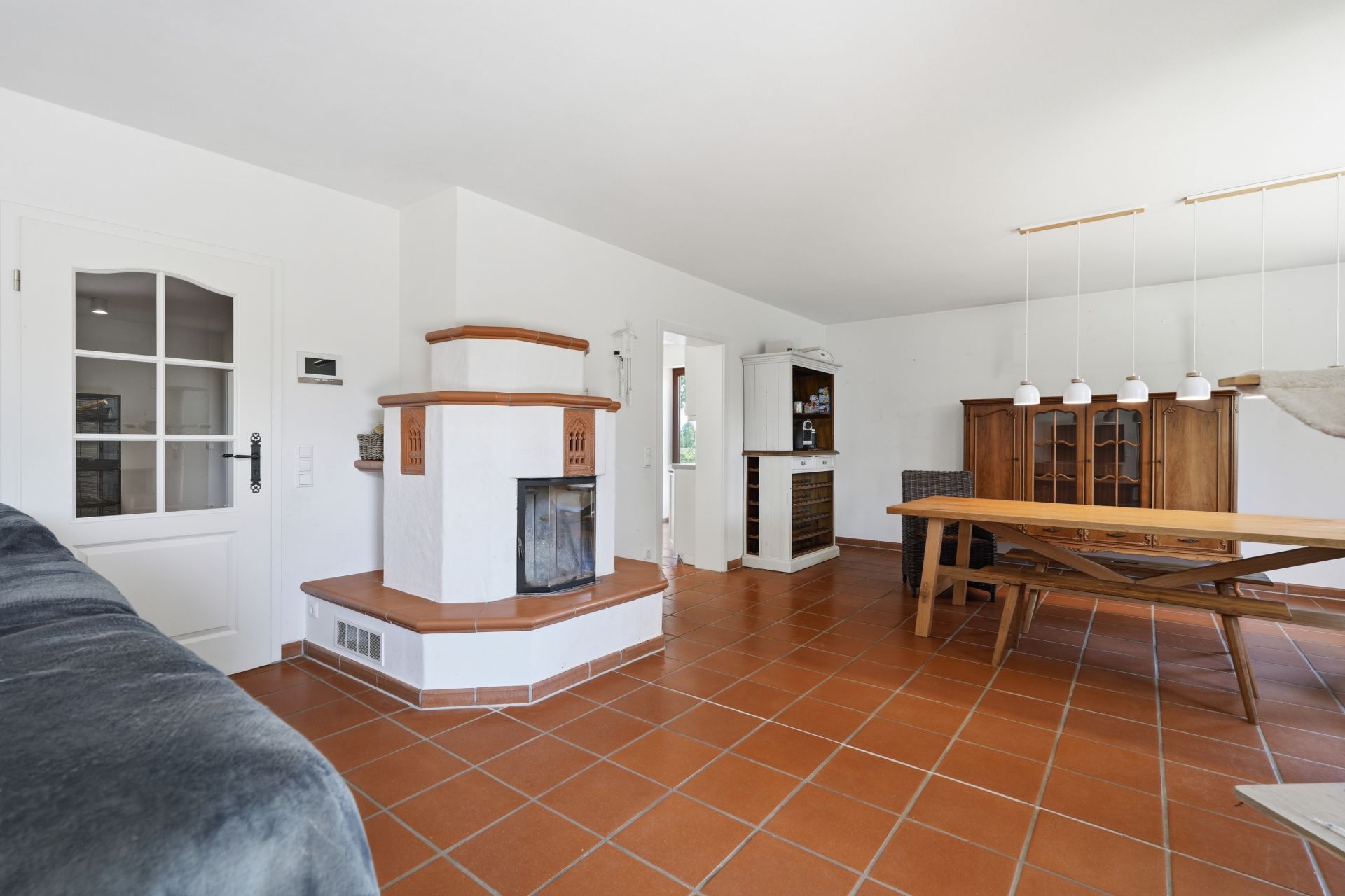Wohnzimmer mit Kamin, Holztisch, Stühlen und braunen Fliesenboden.