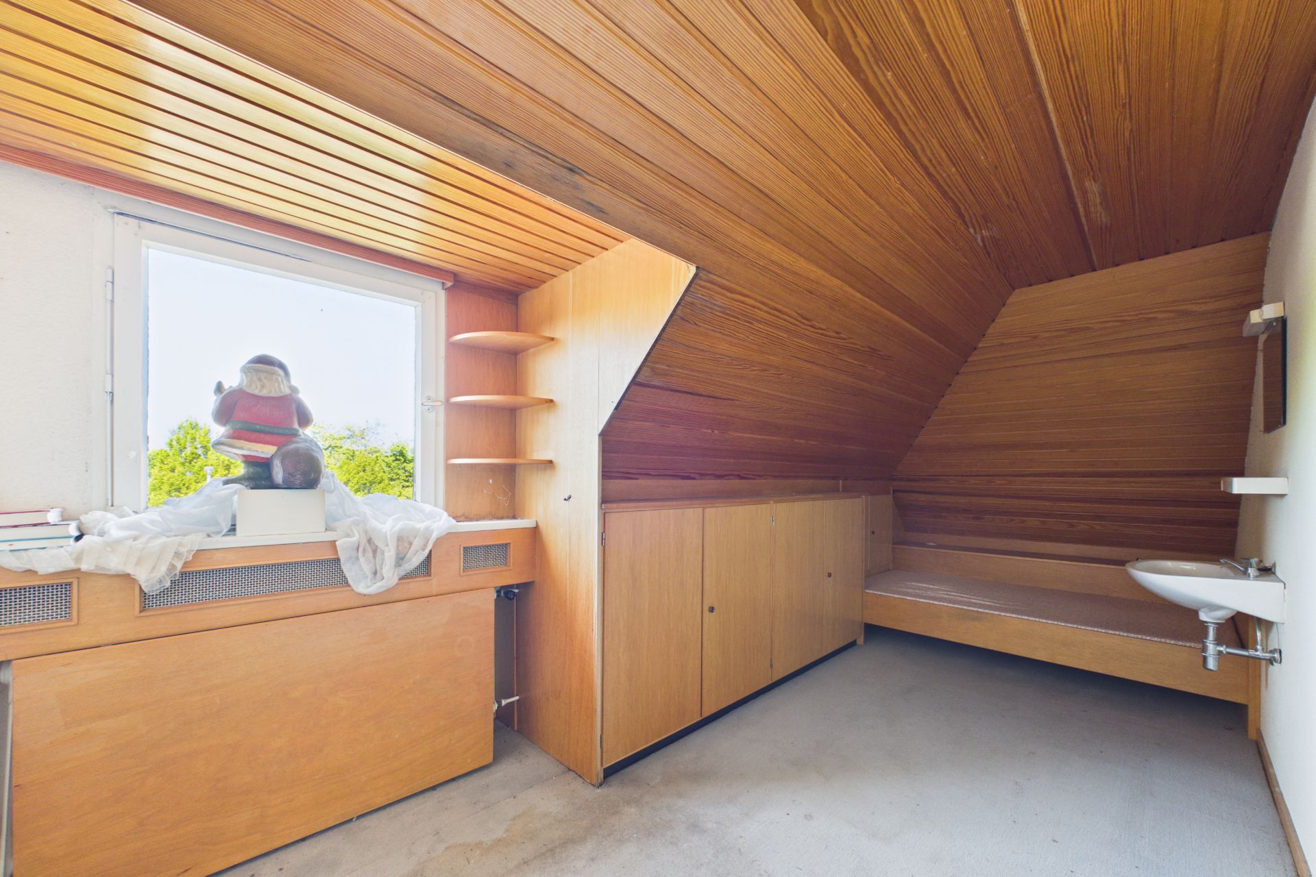 Kleines Zimmer mit Holzdecke, eingebautem Bett, Regal, Waschbecken und Fenster.