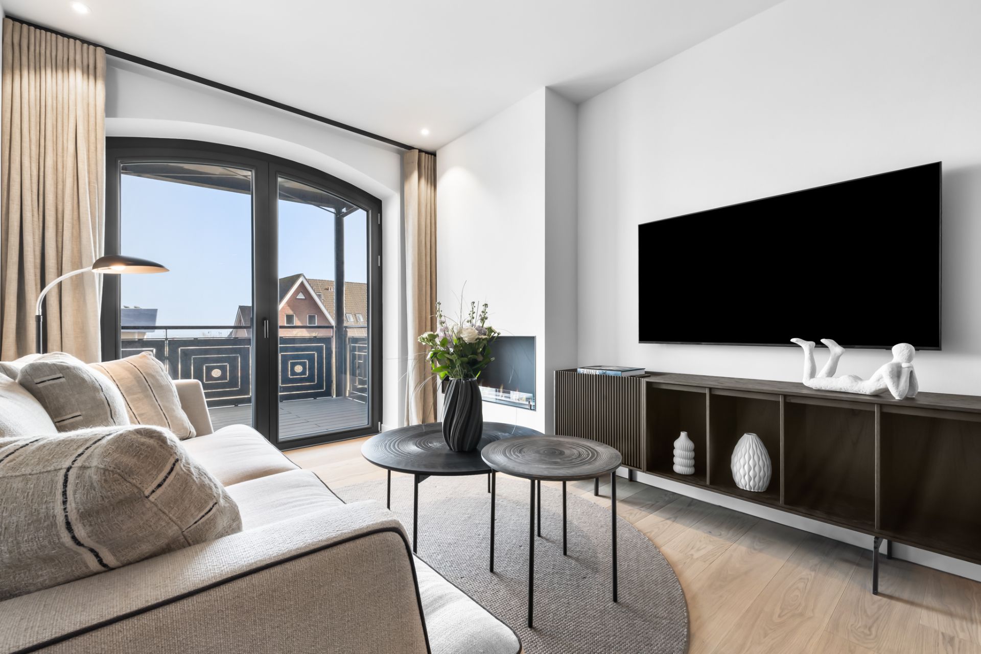 Modernes Wohnzimmer mit Sofa, Couchtischen, großem Fernseher und Balkonfenster.