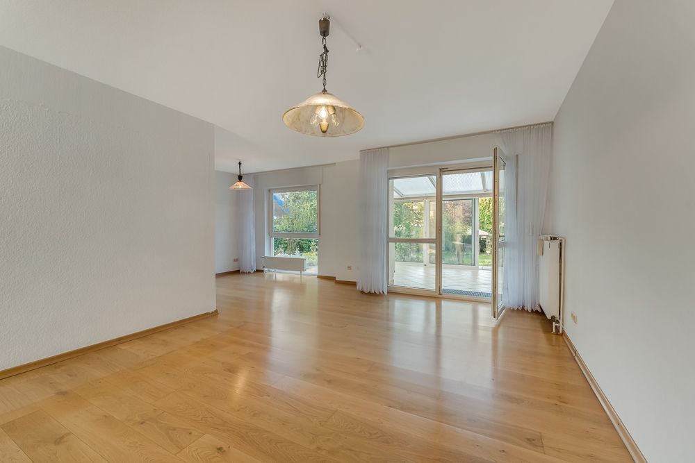 Helles, leeres Wohnzimmer mit Holzfußboden, Hängelampen und Zugang zur Terrasse.