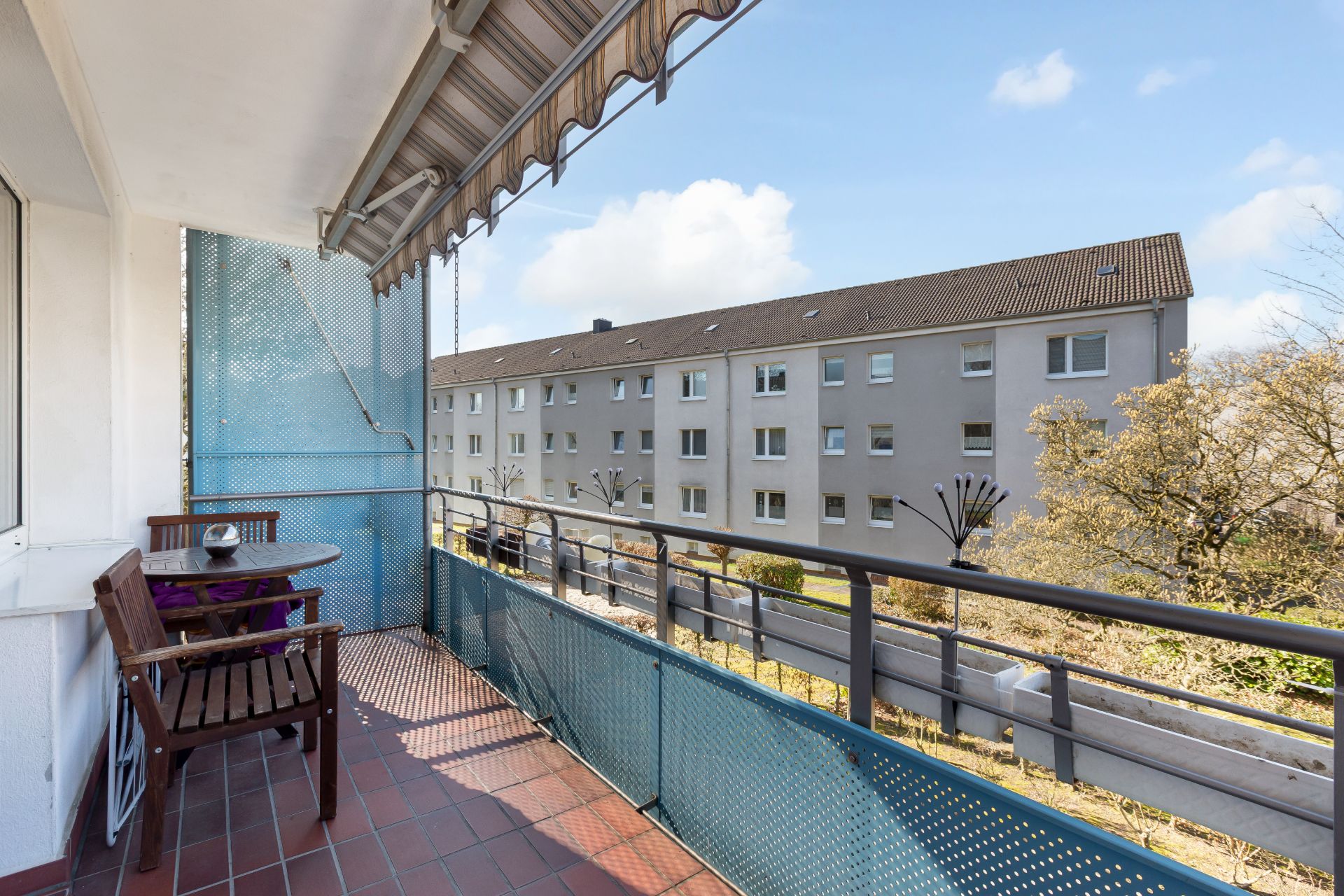 Balkon mit Markise, Tisch und Stühlen, Blick auf Wohnhaus und Bäume.