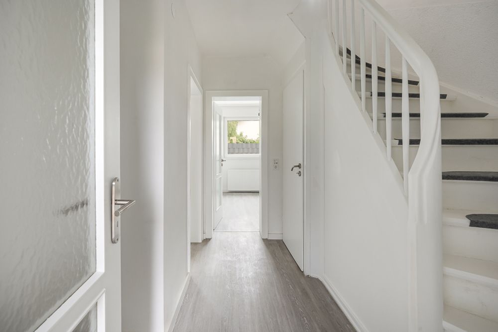Heller Flur mit weißer Treppe und Türen, Blick in ein weiteres Zimmer.