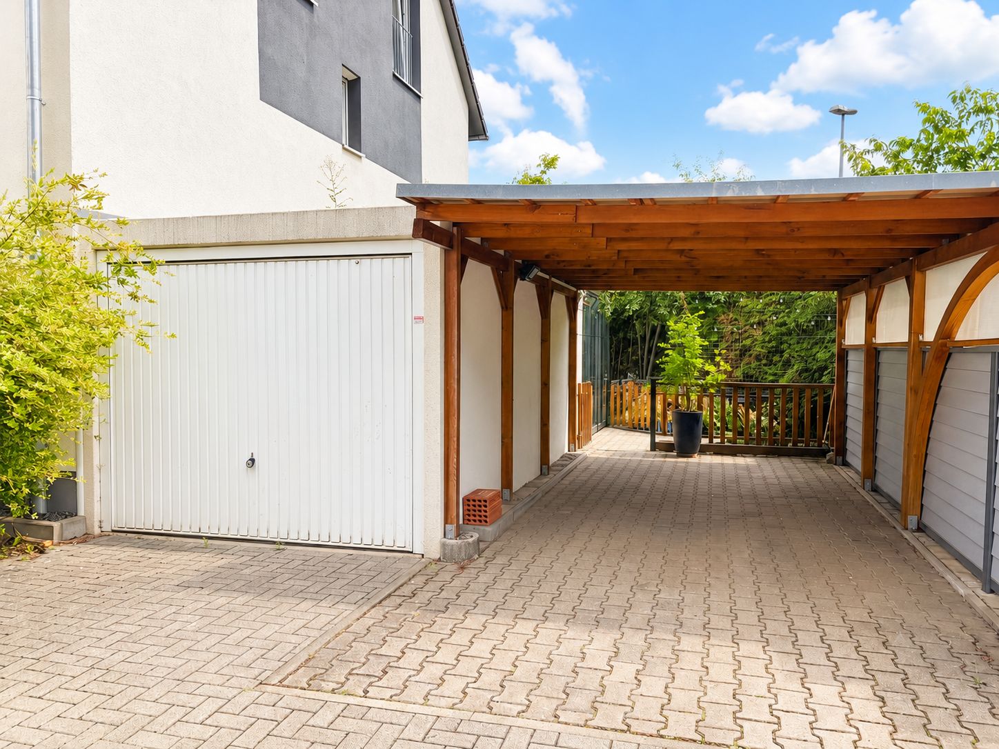Offener Carport mit Holzüberdachung und geschlossener Garage an einem Wohnhaus.