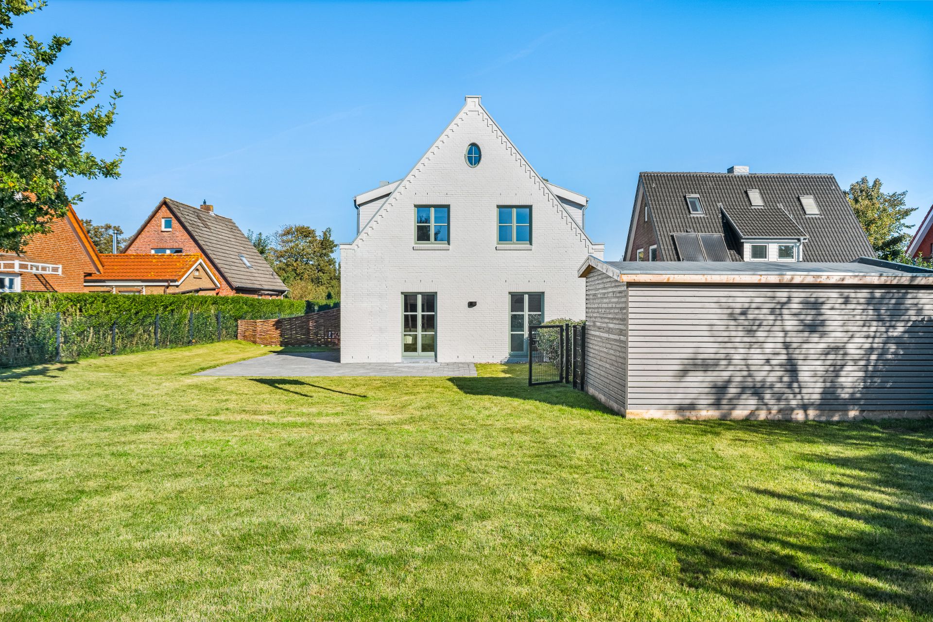 Weißes Einfamilienhaus mit gepflegtem Garten und Nebengebäude an einem sonnigen Tag.