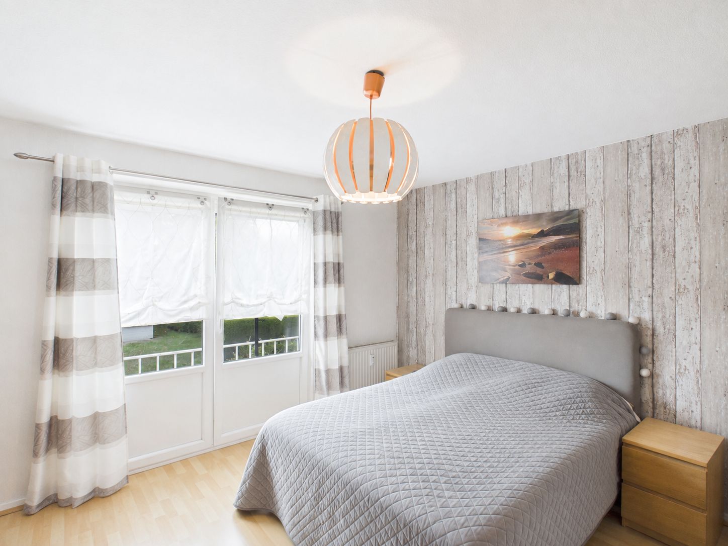 Helles Schlafzimmer mit Doppelbett, Nachttischen, großem Fenster und dekorativer Holzwand.