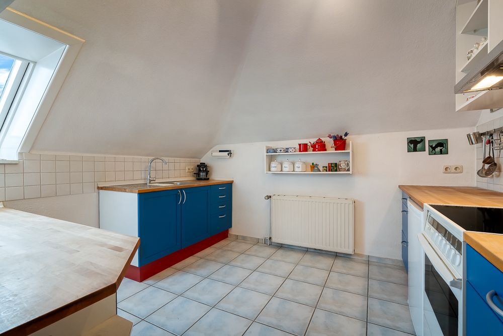 Helle Küche mit blauen Unterschränken, Holzarbeitsplatten und Dachfenster.