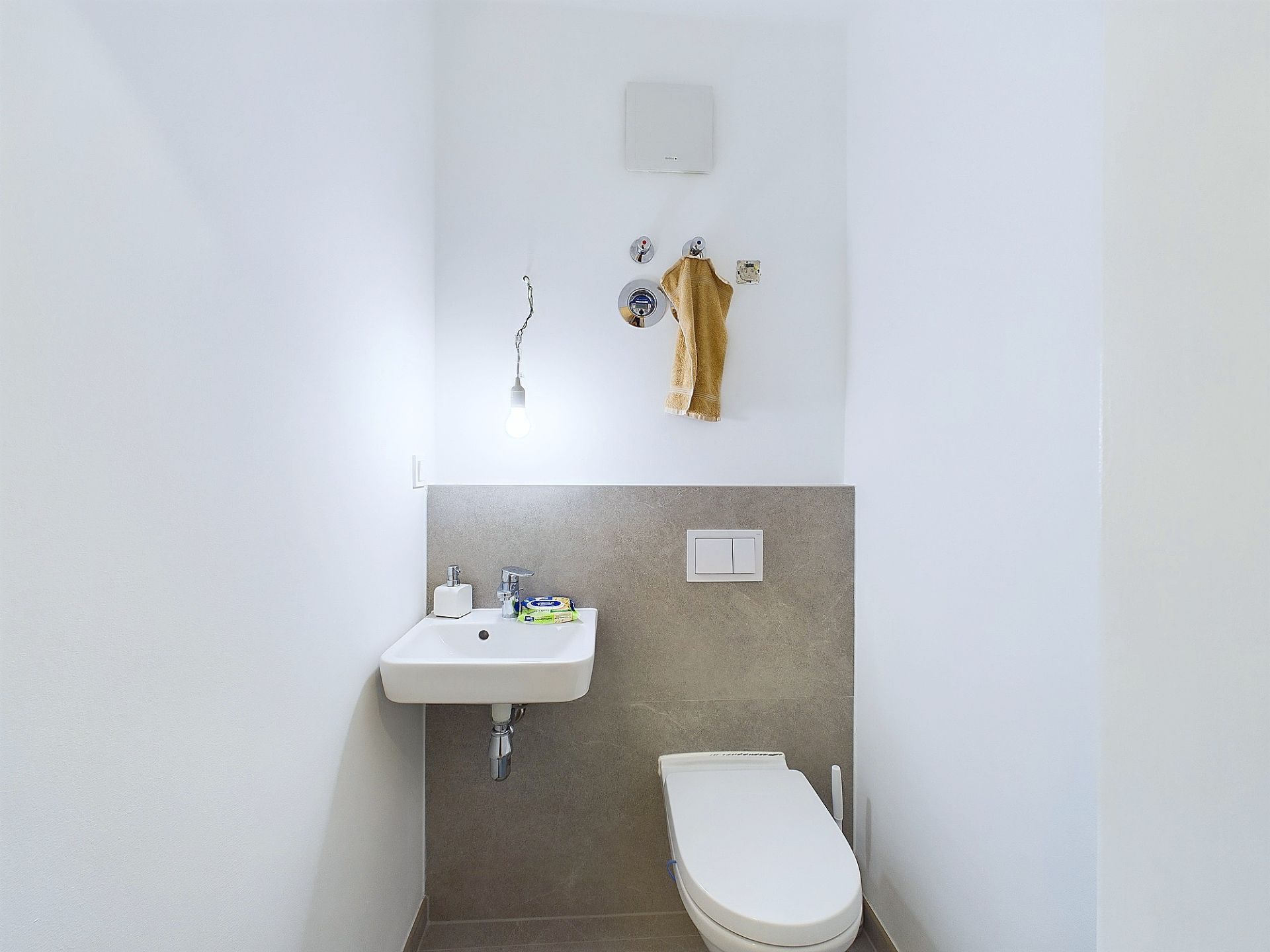Kleines, modernes WC mit Waschbecken und Wandtoilette, hell beleuchtet.