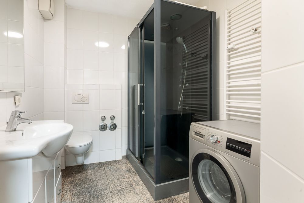 Modernes Badezimmer mit Duschkabine, Waschmaschine, WC und Waschbecken.