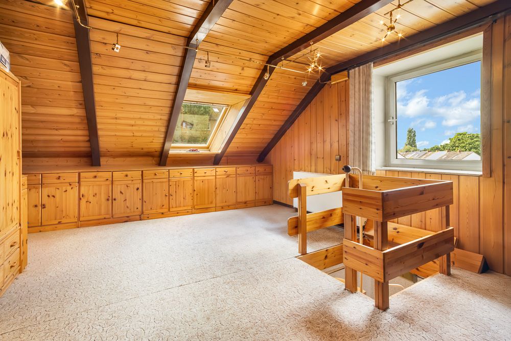 Dachzimmer mit Holzverkleidung, Fenster, Einbauschränken und Treppenaufgang.