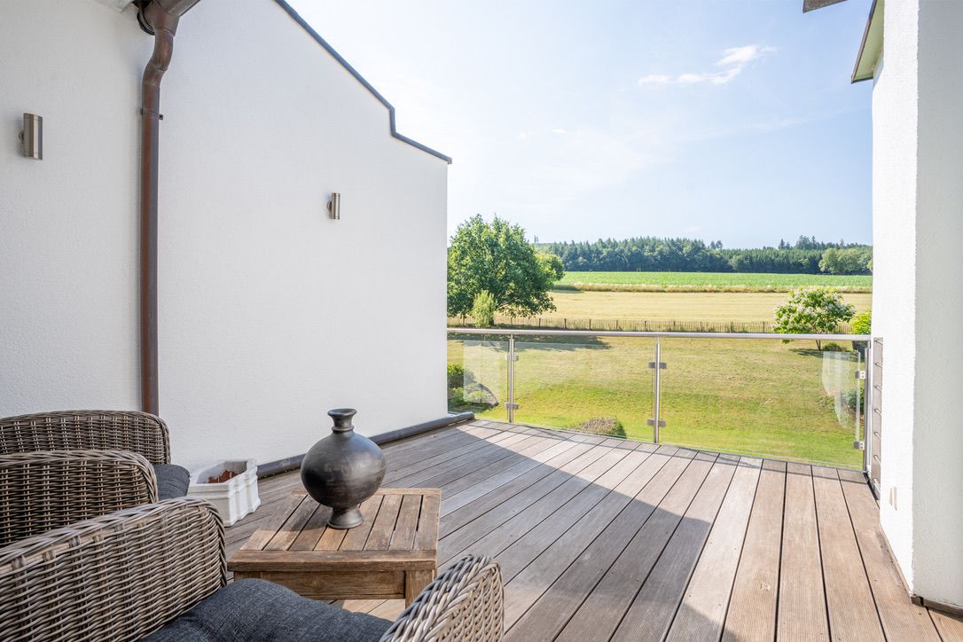 Balkon mit Holzboden, Sitzmöbeln und Blick auf eine Wiese mit Bäumen.