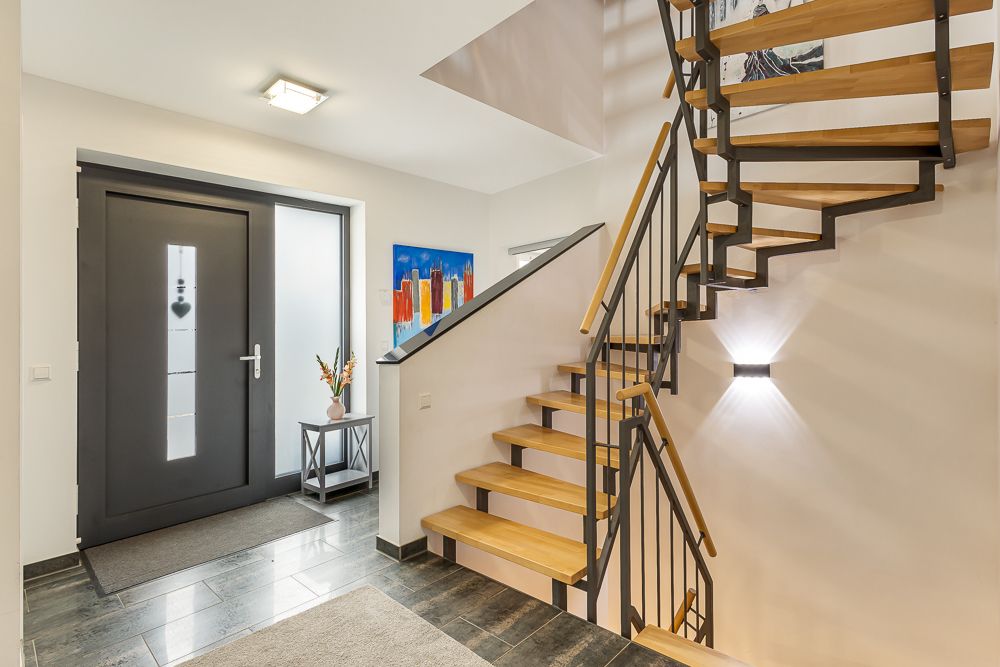 Moderner Flur mit Holztreppe, Glastür, Tisch und farbigem Bild an der Wand.