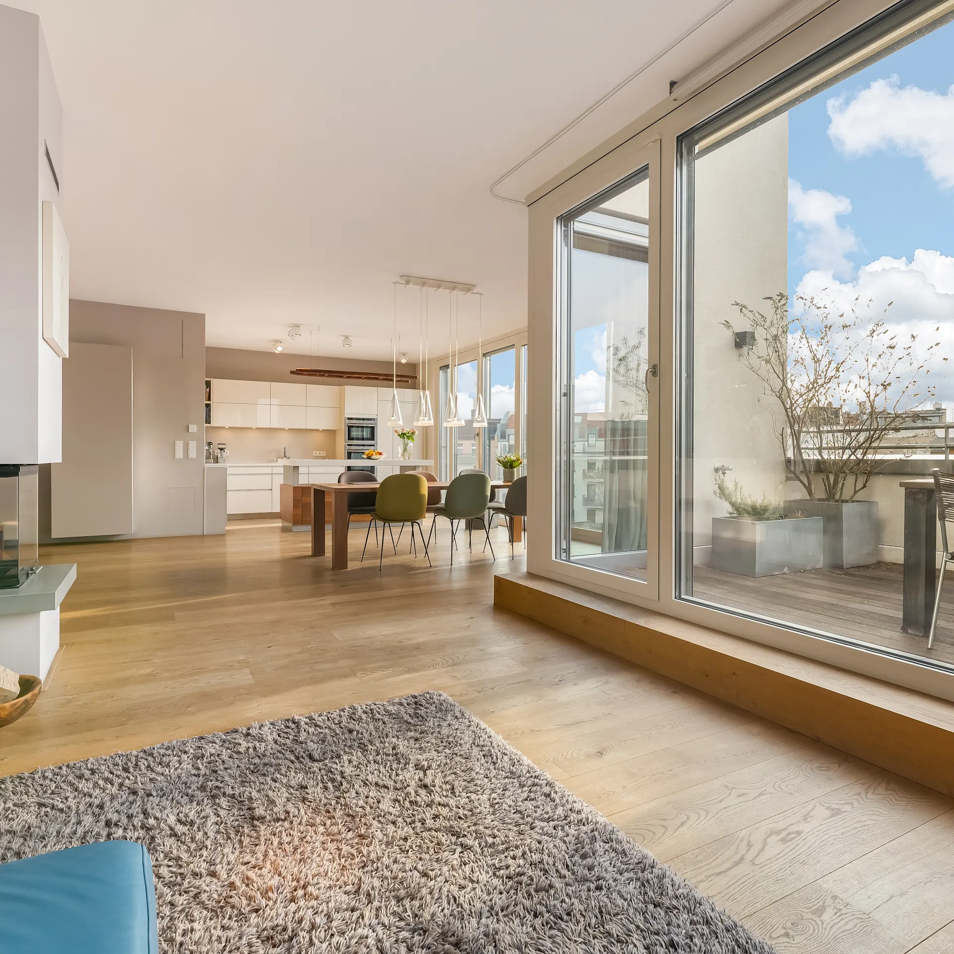 Helles Wohnzimmer mit Kamin, Teppich, Essbereich und Zugang zur Terrasse mit Sitzgruppe.