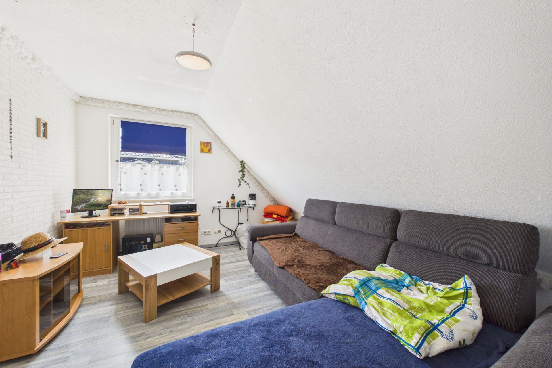Wohnzimmer mit Ecksofa, Couchtisch, Schreibtisch und Fenster mit blauem Rollo.