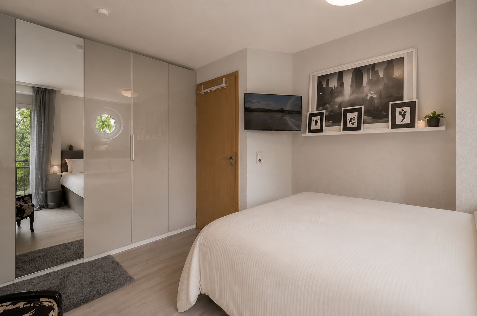 Helles Schlafzimmer mit Doppelbett, Spiegelschrank, Fernseher und Bildern an der Wand.