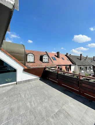 Geräumige Terrasse mit Steinboden und Holzgitter, Blick auf Nachbarhäuser mit roten Dächern.