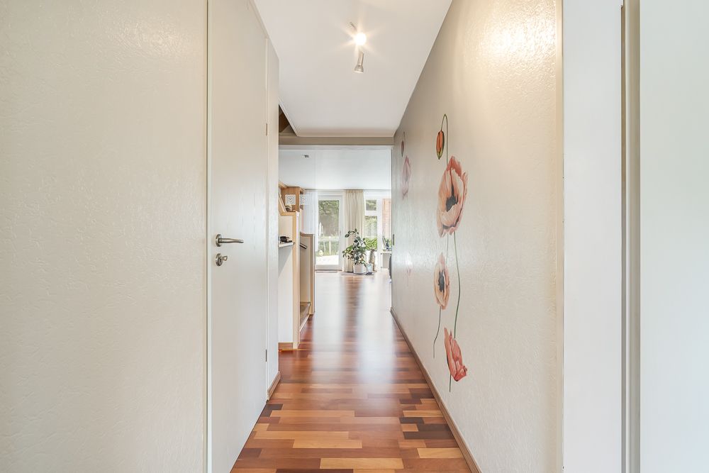Heller Flur mit Holzboden und Blumenwandmalerei, Blick Richtung Wohnzimmer mit Pflanzen.