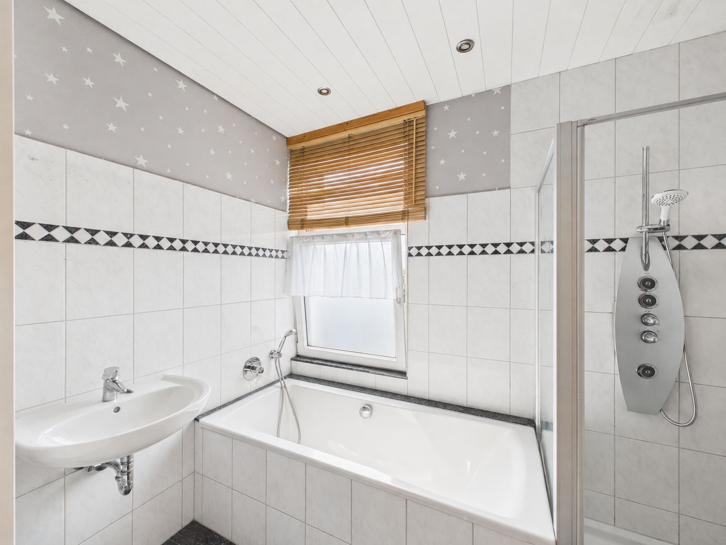 Helles Bad mit Badewanne, Dusche, Waschbecken und Fenster mit Jalousie.