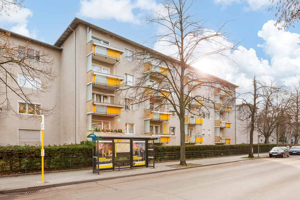 Mehrstöckiges Wohnhaus mit gelben Balkonen und Bushaltestelle davor.