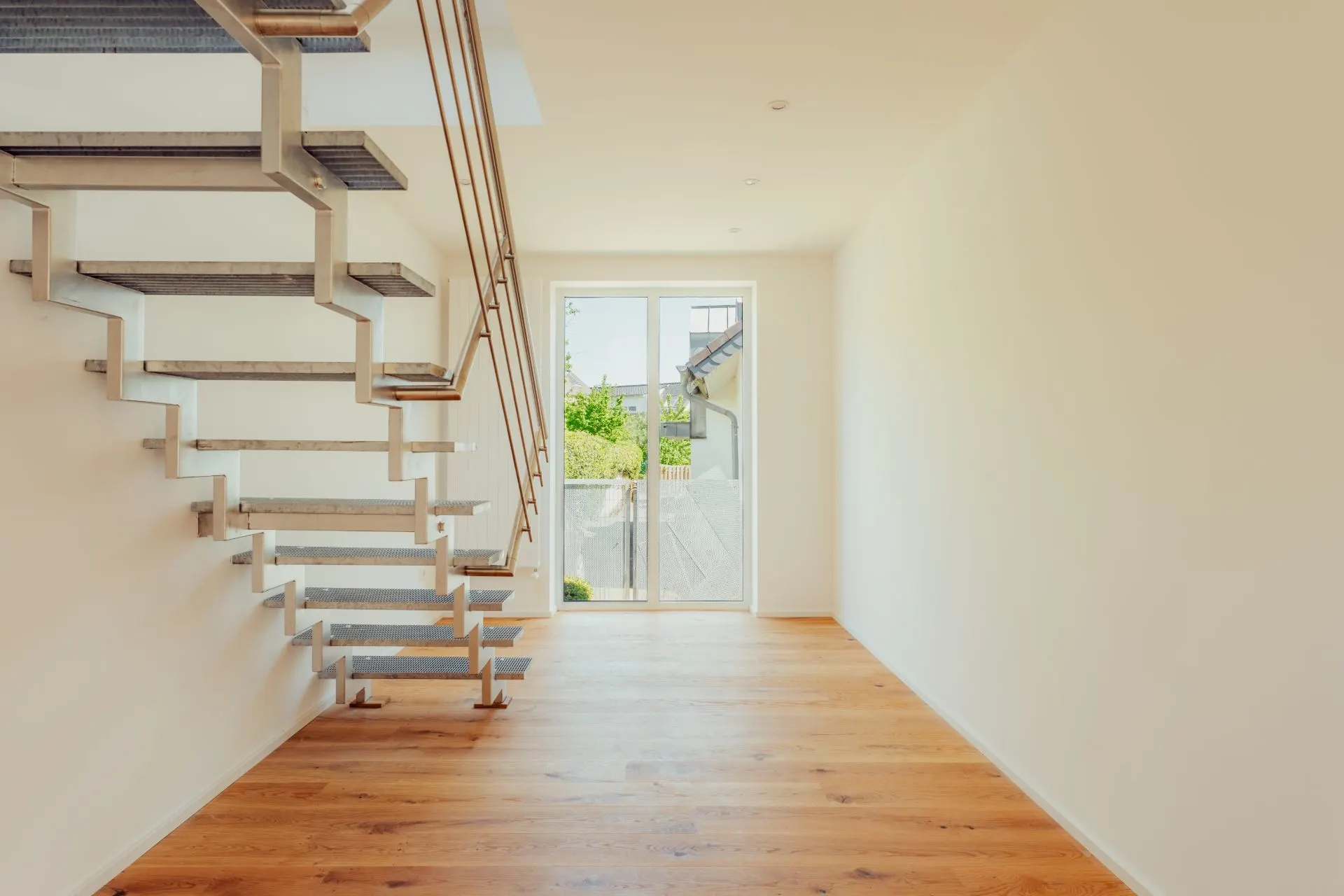 Heller Raum mit Holzfußboden, moderner Metalltreppe und bodentiefem Fenster.