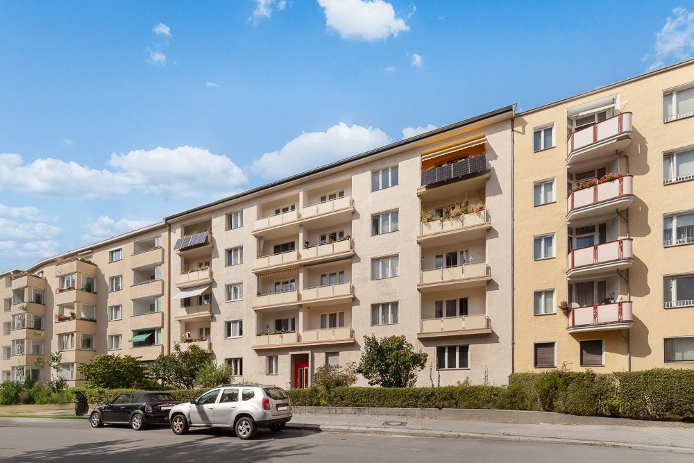 Mehrstöckiges Wohnhaus mit Balkonen und parkenden Autos davor.