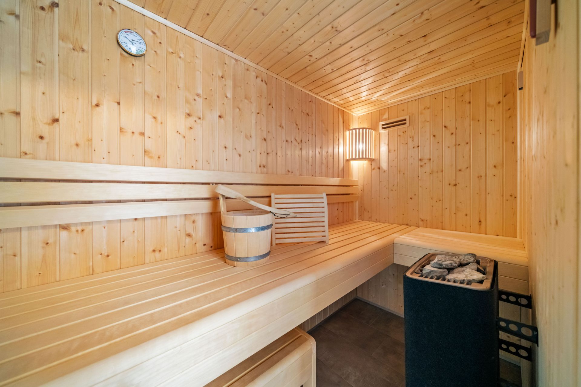 Holzsauna mit Bank, Eimer, Saunaofen und Wanduhr, warm beleuchtet.