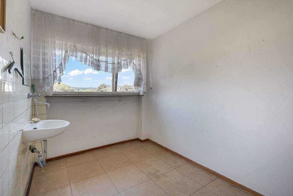 Leerer Raum mit kleinem Waschbecken und Fenster mit Vorhang.