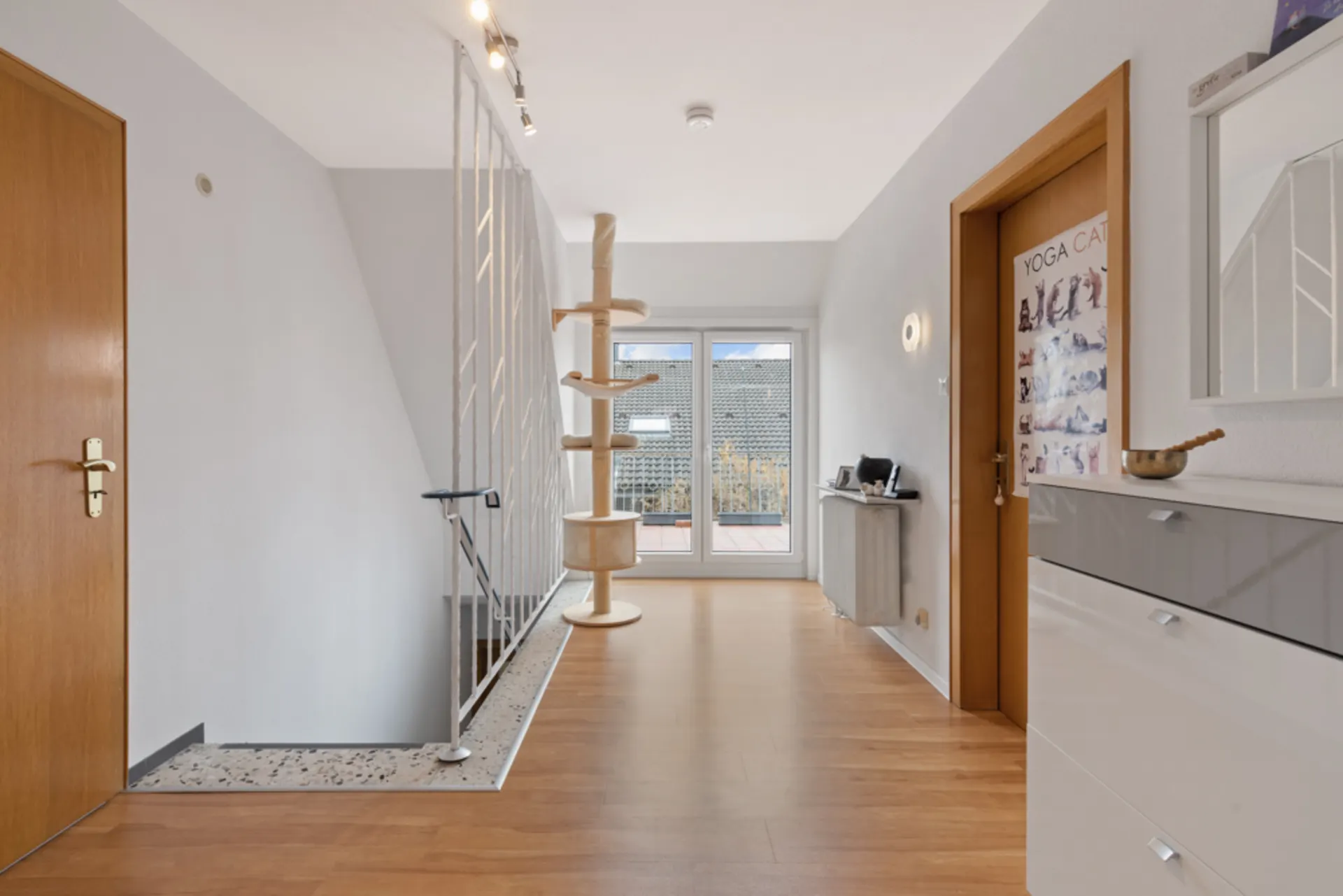 Heller Flur mit Holzfußboden, Katzenbaum, Türen und großem Fenster zum Balkon.
