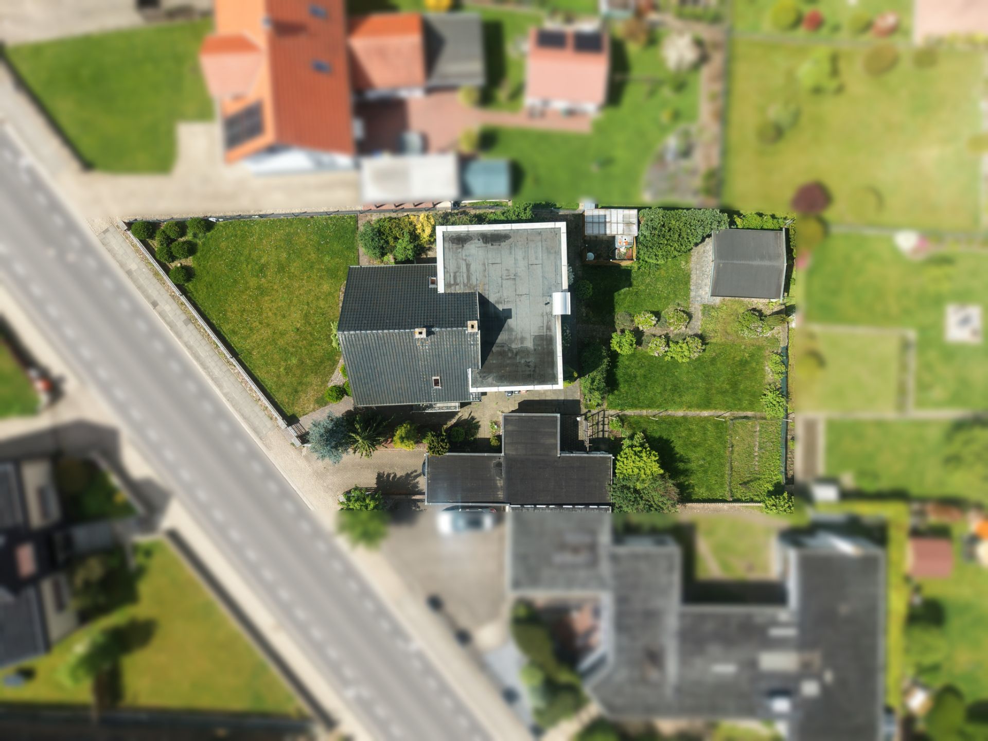 Luftaufnahme eines Einfamilienhauses mit Garten und angrenzender Straße.
