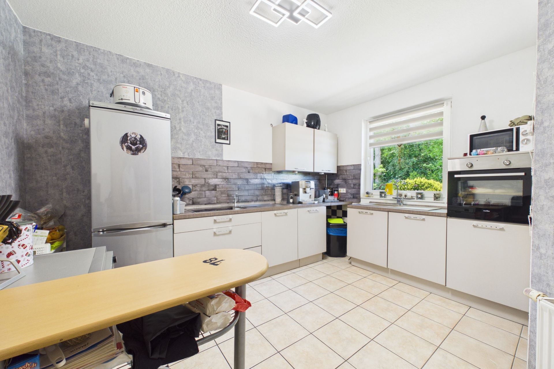 Moderne Einbauküche mit Kühlschrank, Herd, Fenster und Fliesenboden.