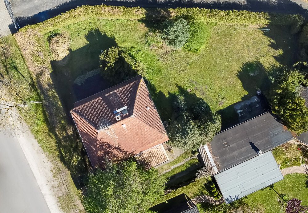 Luftaufnahme eines Hauses mit rotem Dach und großem Garten, umgeben von Bäumen und Wiese.