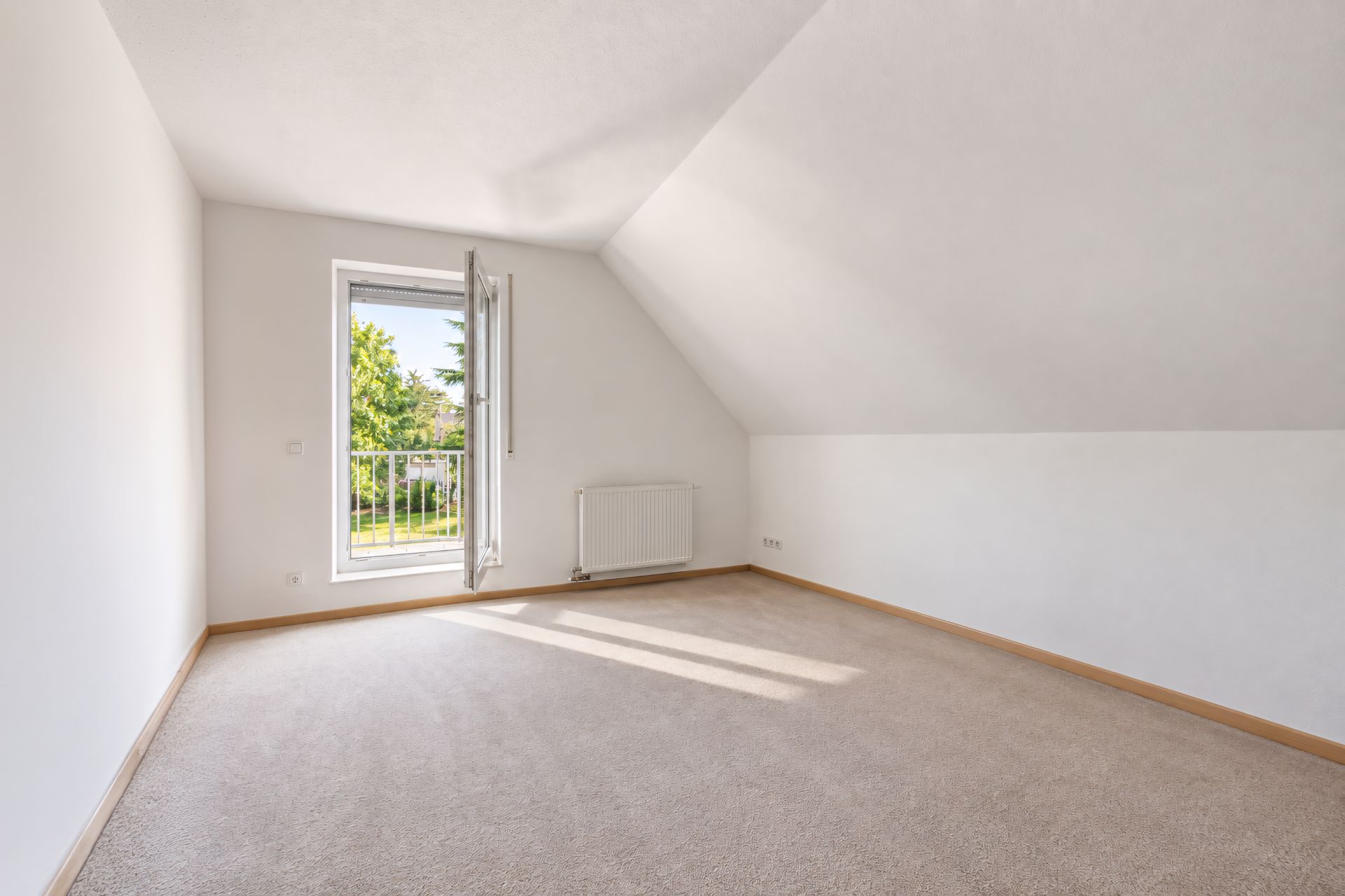 Helles Zimmer mit Teppichboden, Dachschräge, offenem Fenster und Blick ins Grüne.