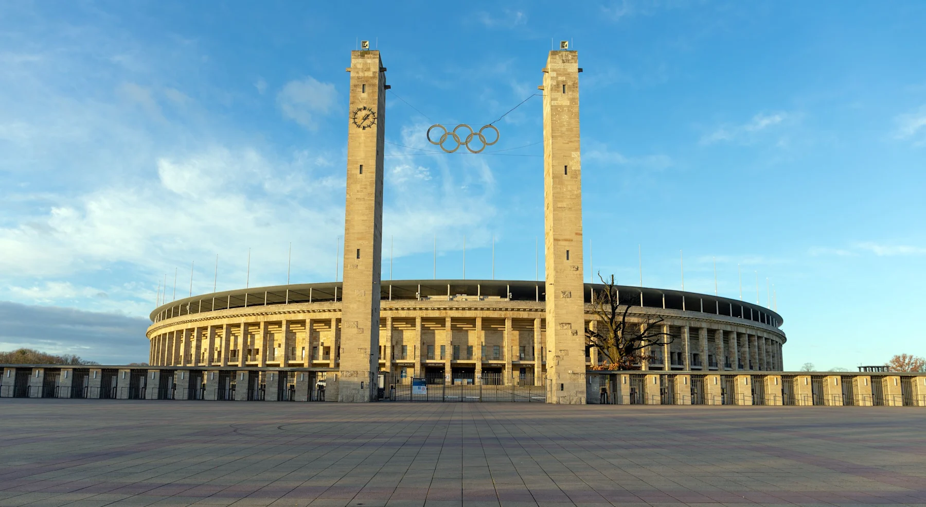 Großes rundes Stadion mit zwei hohen Steinsäulen und Olympischen Ringen vorne.