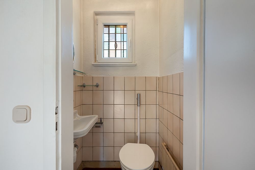Kleines Badezimmer mit Toilette, Waschbecken und kleinem Fenster mit buntem Glas.