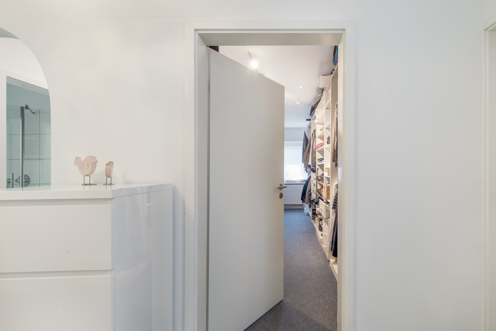 Blick durch eine offene Tür in einen begehbaren Kleiderschrank mit Regalen.