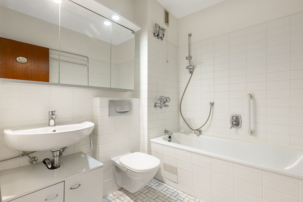 Helles Badezimmer mit Badewanne, Dusche, Waschbecken, Spiegel und Toilette.