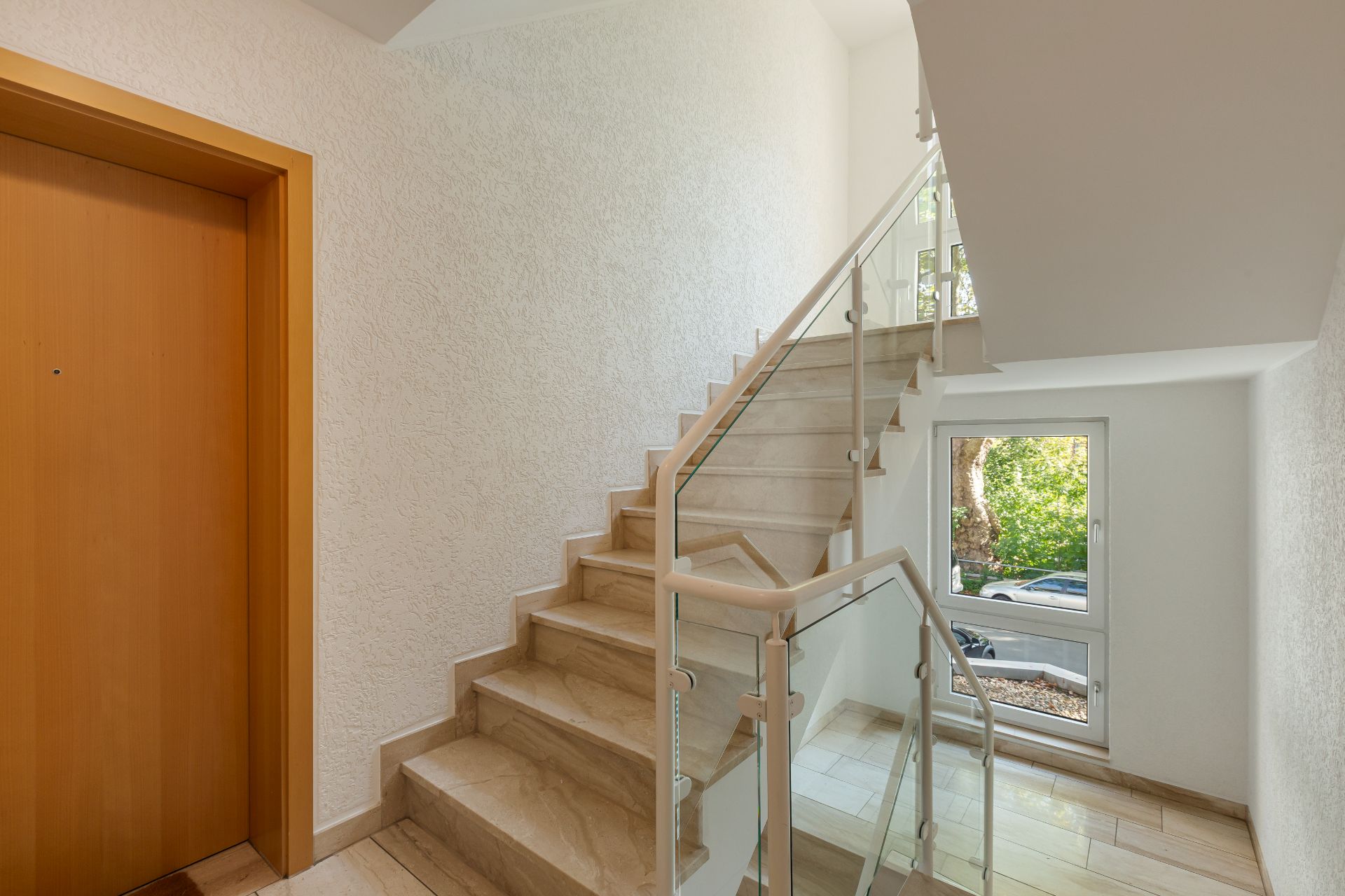 Treppenhaus mit Aufzug, Marmortreppe und Fenster mit Blick ins Freie.