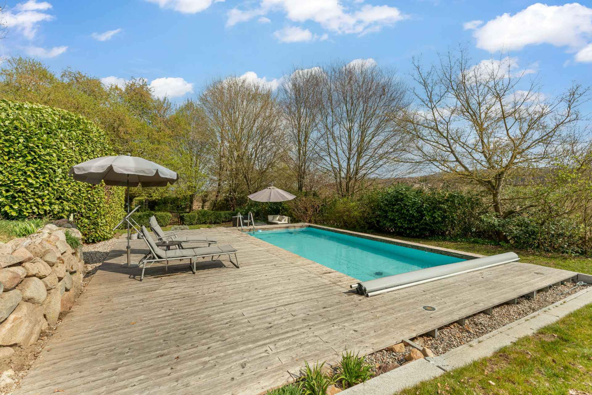 Holzterrasse mit Pool, Liegestühlen und Sonnenschirmen im Garten.