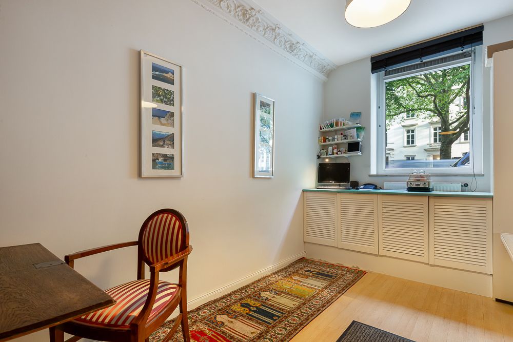 Kleines Arbeitszimmer mit Schreibtisch, Stuhl, Teppich und großem Fenster mit Blick nach draußen.