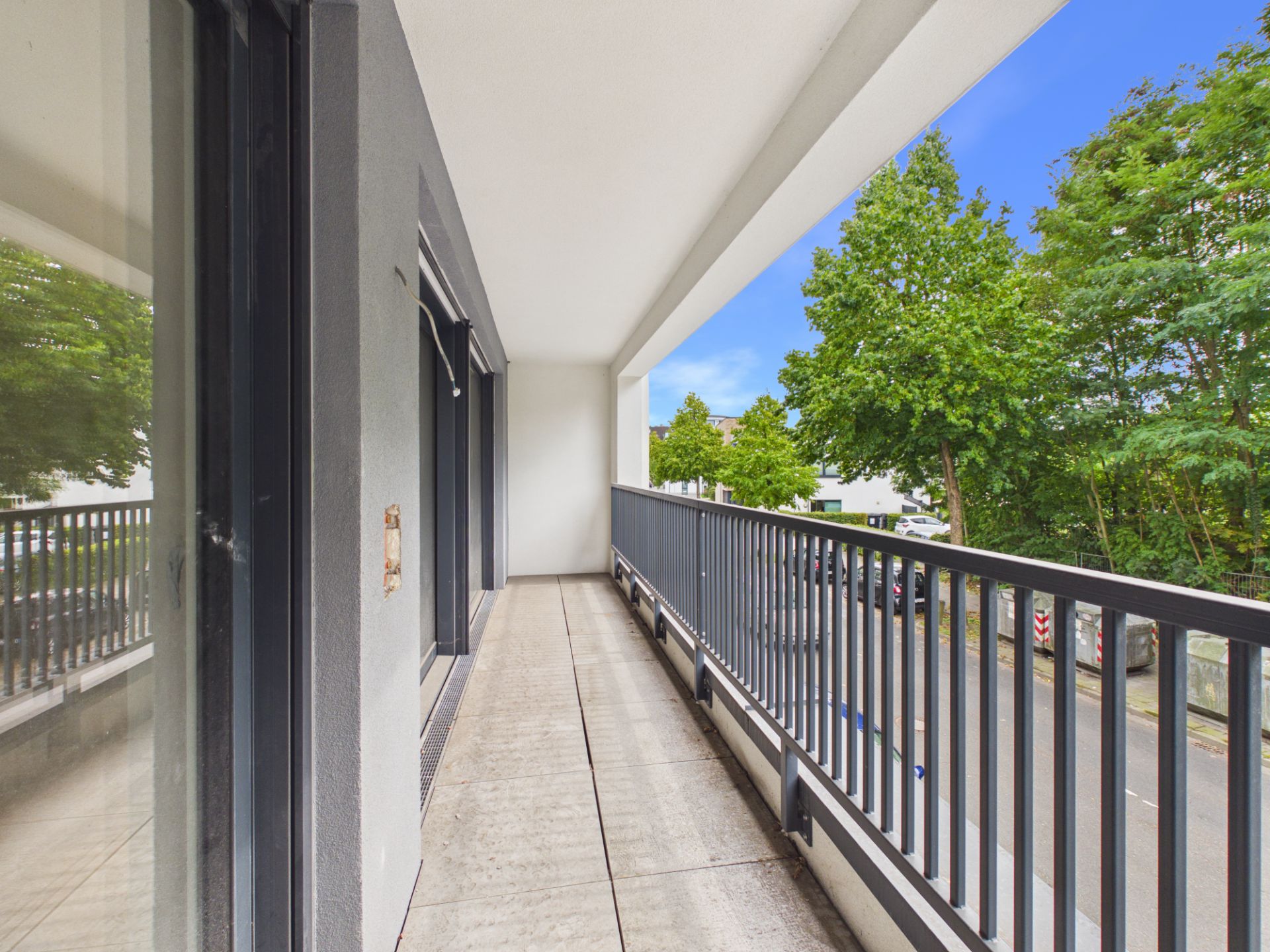 Langer Balkon mit Metallgeländer und Blick auf eine Straße und Bäume.